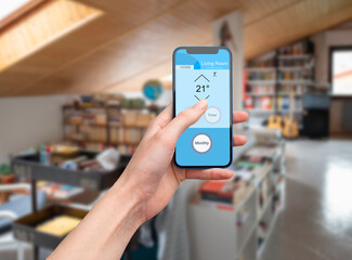 Hand holding a mobile phone showing an home automation app to manage smart technology in a modern...