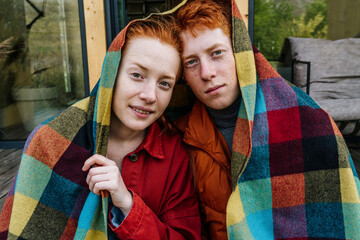 Heterosexual couple wrapped in blanket sitting on house deck