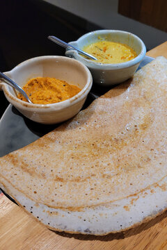 A plate of dosa also known as thosai or tosai with dipping sauce. A dosa is a thin crepe originating from South India, made from a fermented batter predominantly consisting of lentils and rice.