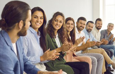 Obraz premium Group of men and women sit in a row and applaud a man who puts forward an idea or says something. People communicate at a business meeting or meet with competitors, standing in line for an interview.
