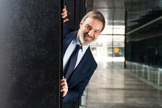 Happy Businessman Peeking From Behind Black Column