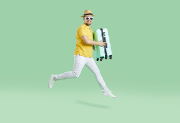 Cheerful male tourist in summer clothes running with suitcase on light green background. Funny millennial man rushes on summer tourist flight. Summer vacation concept. Banner. Full length.
