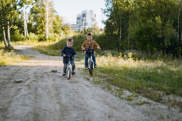 cute caucasian boys brothers are cycling together in countryside in summer time. Little one is riding runbike, elder one riding bicycle. Image with selective focus