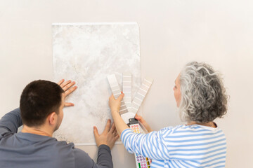 Woman and friend choosing from wallpaper sample and color catalog on wall