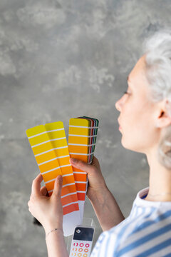 Woman choosing color from swatch chart in front of wall