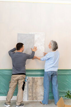 Woman and friend choosing wallpaper from samples on white wall