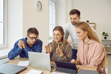 Happy smart university students sitting at campus library desk, doing group project, cooperating, planning research, discussing idea and strategy, preparing presentation on laptop and tablet computer