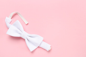 Stylish white bow tie on pink background, top view. Space for text