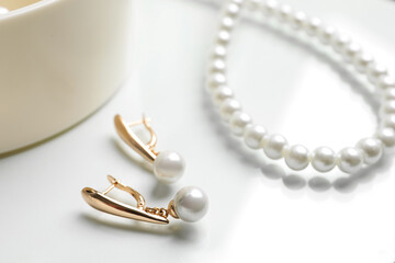 Elegant golden earrings and necklace with pearls on white table, closeup