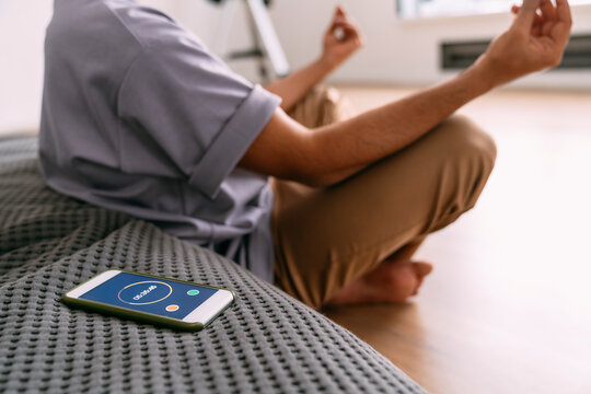 Young man meditating by smart phone with timer at home
