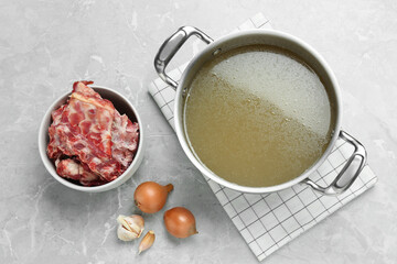 Pot with delicious bone broth and ingredients on light grey table, flat lay