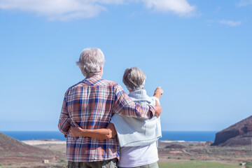Rear view of mature active senior couple hiking in mountain range enjoying healthy lifestyle and sunny day. Two smiling elderly people during vacation, horizon over water.