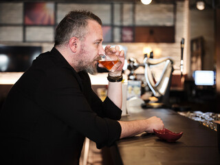 Portrait of a handsome mature man drinking a glass of neat whiskey at the bar or pub.