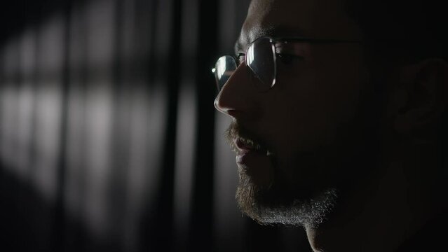 Man puts on his glasses and looks away. Shot from the film. A man's face against a dark background. 