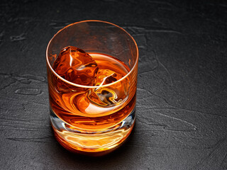 Glass of elegant whiskey with ice on a textured black background with hard light.