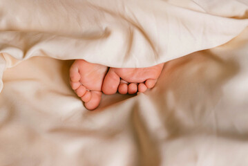 Children's feet on a white bed. Infant baby is sleeping in his crib. Importance of sleep for...