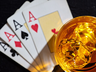 Glass of whiskey with ice cubes on poker playing cards with four aces. Poker game gambling and whisky
