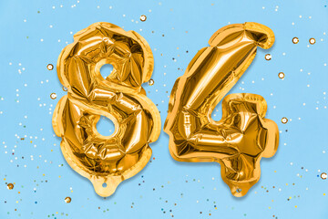 The number of the balloon made of golden foil, the number eighty-four on a blue background with sequins. Birthday greeting card with inscription 84. Numerical digit. Celebration event, template