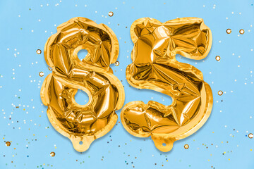 The number of the balloon made of golden foil, the number eighty-five on a blue background with...