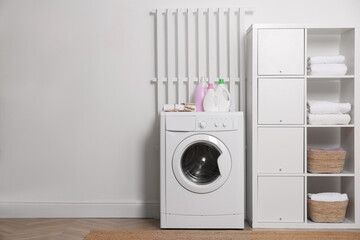 Laundry room interior with modern washing machine and shelving unit near white wall