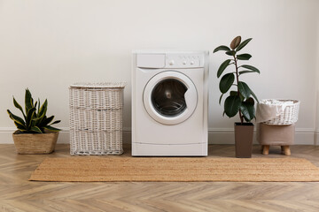Laundry room interior with modern washing machine and wicker basket near white wall - obrazy, fototapety, plakaty