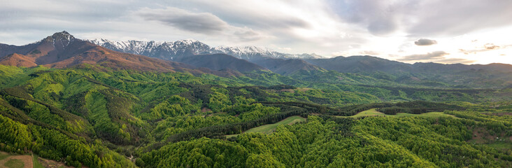 Naklejka na ściany i meble Amazing panoramic view from a drone of the mountain with snow peaks and green hills.