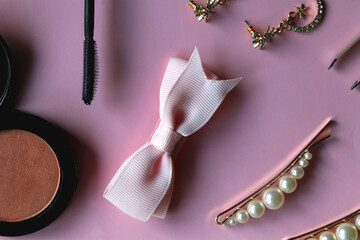 Pink scrunchie, gold earrings and rings, blush, various hair barrettes, lipstick and jade roller on bright pink background. Flat lay.