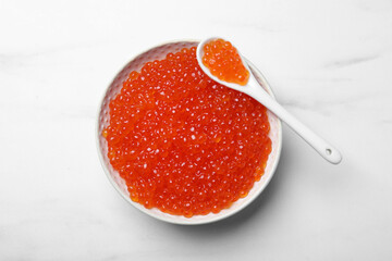Bowl and spoon with delicious red caviar on white table, top view