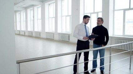 Businessman is talking to realtor about terms renting an office space, front view. Real estate agent with tablet in hands discusses with client terms of lease of premises