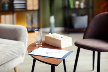 Clipboard with blank sheet, glass of water and napkin box on table in office of therapist