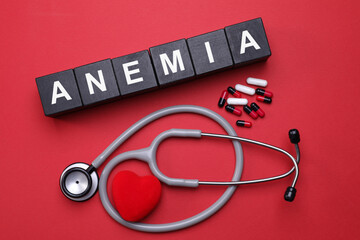 Word Anemia made with black wooden cubes, pills, stethoscope and decorative heart on red background, flat lay