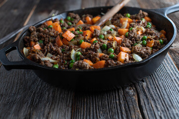 Pan fried ground beef with peas and carrots in a cast iron pan