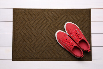 New clean door mat with shoes on white wooden floor, top view