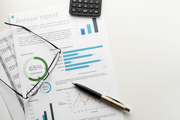 Mockup annual report sheet with charts and graphs, pen, calculator and eyeglasses on white desk. Accounting, business, finance, tax and office concepts with copy space.