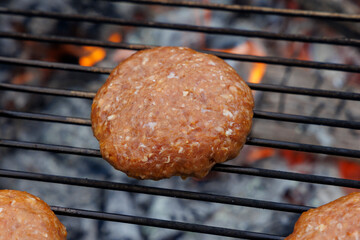 Homemade crispy fried hamburger patties on the grate of a charcoal grill over glowing coals with small flames