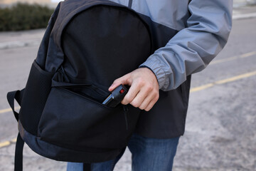 Man putting pepper spray into backpack outdoors, closeup