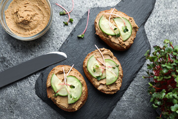 Slices of bread with delicious pate, cucumber and microgreens on grey table, flat lay