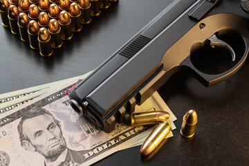 9 mm semi-automatic pistol and full metal jacket bullets on dollar banknotes laid out on black table. Conceptual mockup of gun control, crime, military-industrial complex or defense.