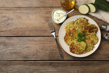 Delicious zucchini fritters served on wooden table, flat lay. Space for text