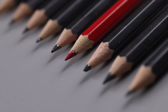 One red pencil between row of black pencils