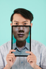 Young Asian man holding tablet computer with his portrait on screen