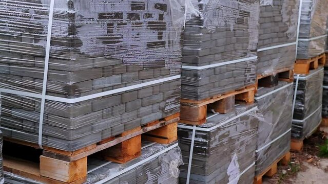 Huge packs of grey bricks stacked at wooden pallets. Construction materials covered with cellophane and tied with plastic band.