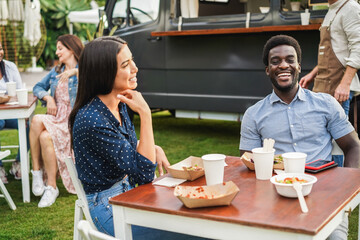 Multiracial couple having fun eating at food truck restaurant outdoor - Focus on african man face