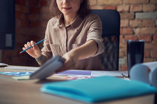 Cropped shot of interior designer smiling, holding pencil and working with color samples, sitting at the desk in her office