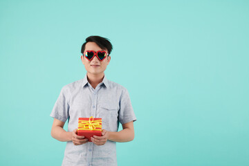 Smiling young man in heart shape sunglasses holding wrapped gift for Valentines day or birthday