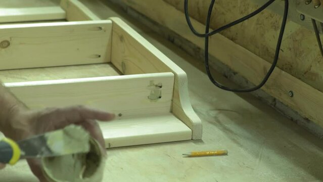 A mature carpenter makes a shelf in his carpentry workshop, works with a tool with wood