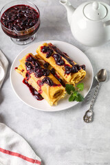 Rolled pancakes with honeysuckle jam on a plate with a mint leaf