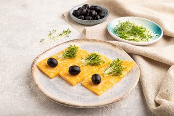 Marble cheese with olives and watercress microgreen on gray concrete. side view, close up.