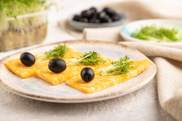 Marble cheese with olives and watercress microgreen on gray concrete. side view, selective focus.
