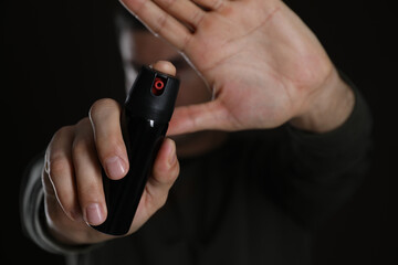 Man using pepper spray against black background, focus on hands